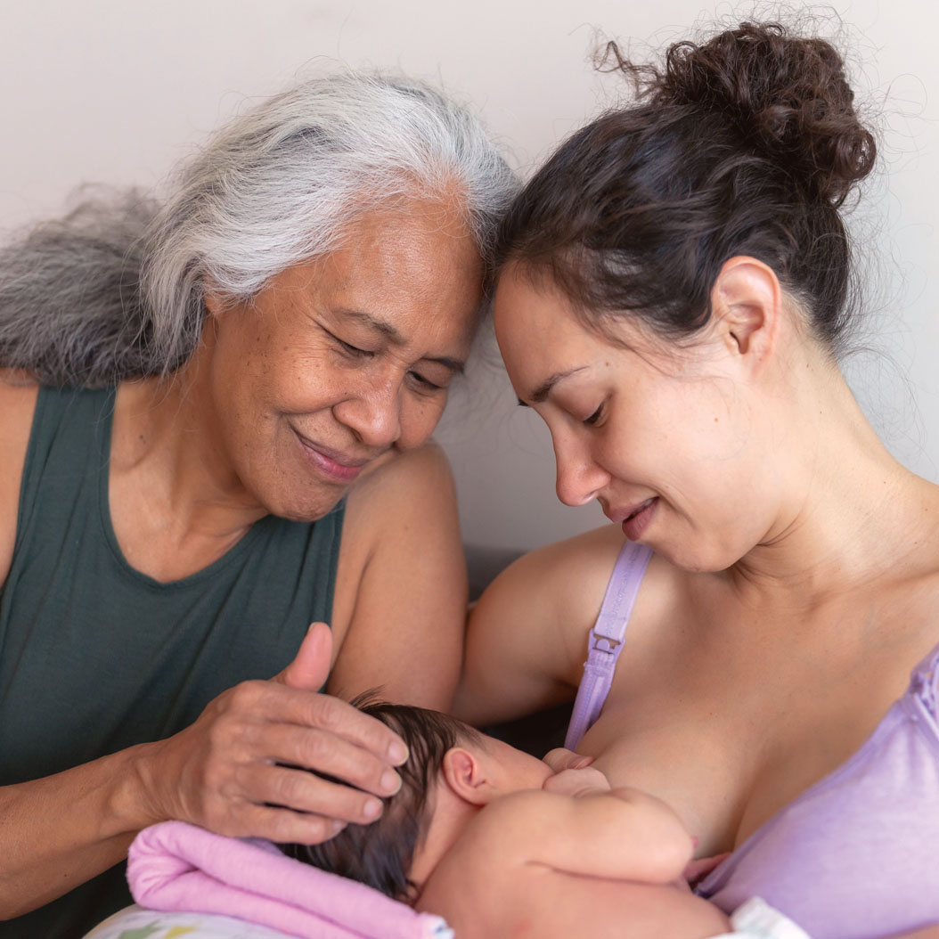 A new young mother gets encouragement from her mom while breastfeeding her infant daughter