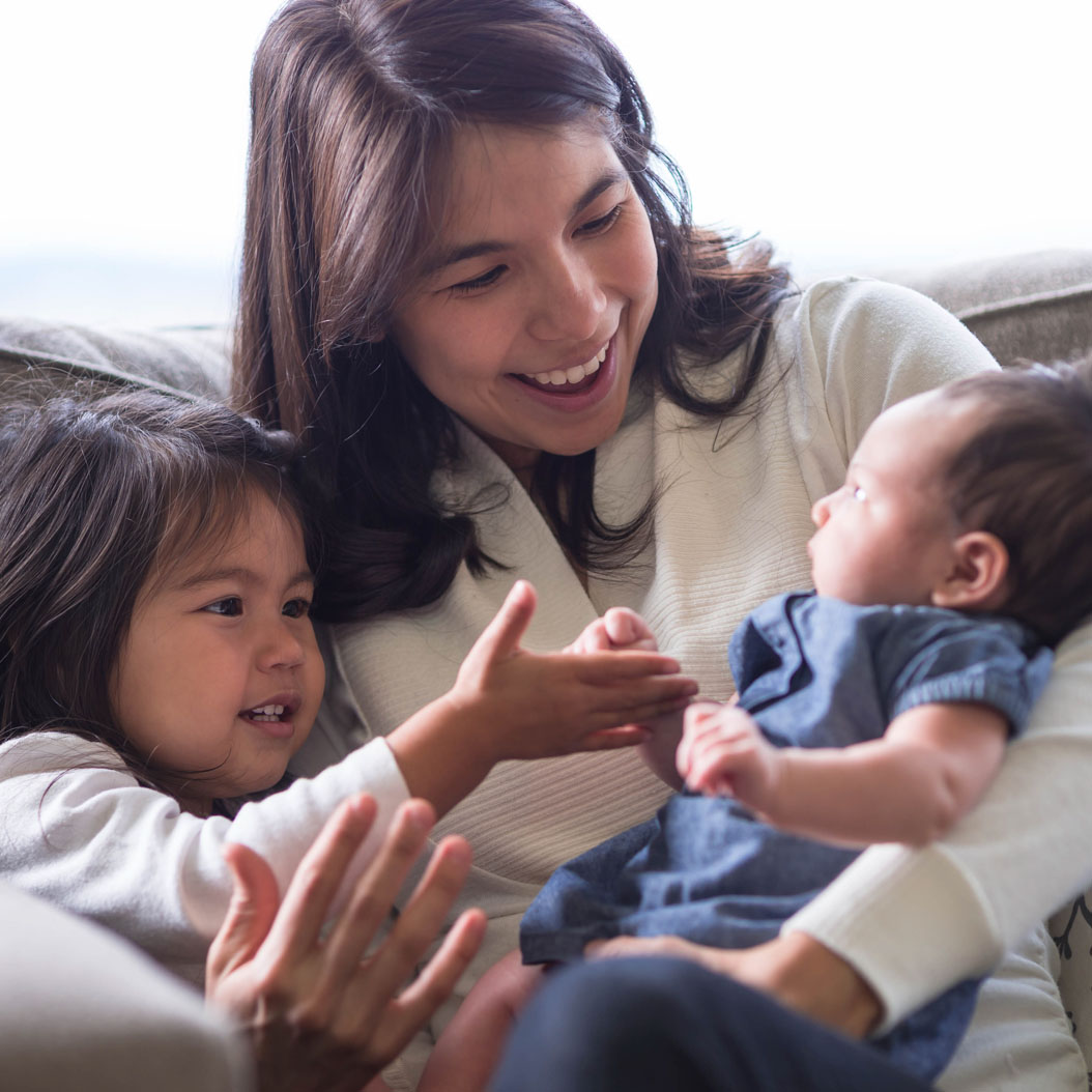Mom sitting with daughter and holding new baby