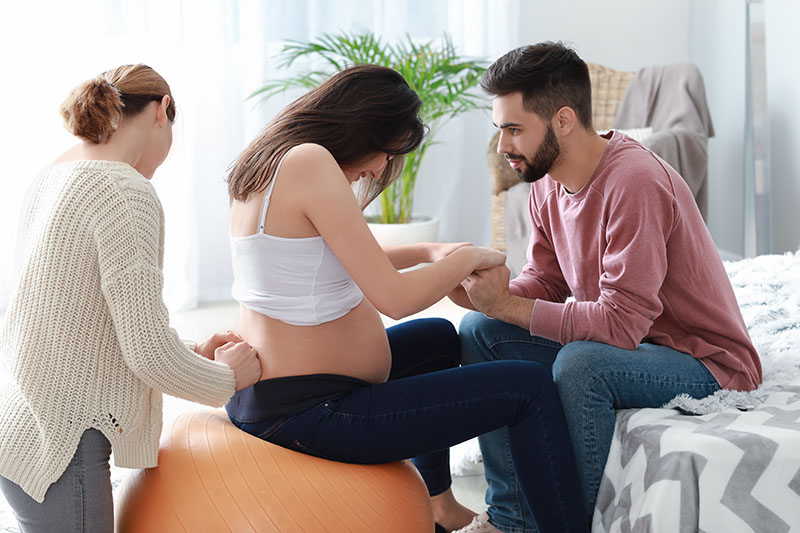 Partner and doula helping a mom with pain management during labor without medication using an exercise ball and massage.