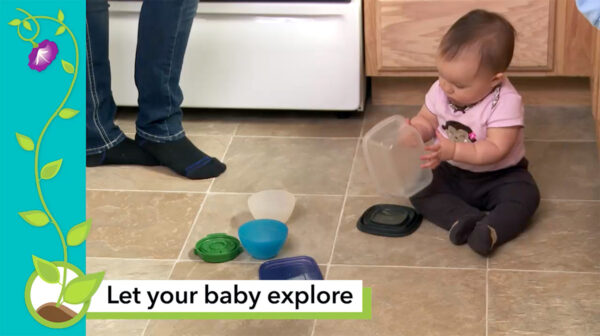 A baby plays with plastic food containers on the kitchen floor with a parent close by.