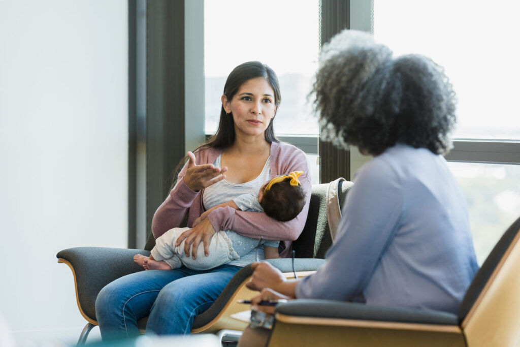 A mother holding her newborn talking to a mental health professional.