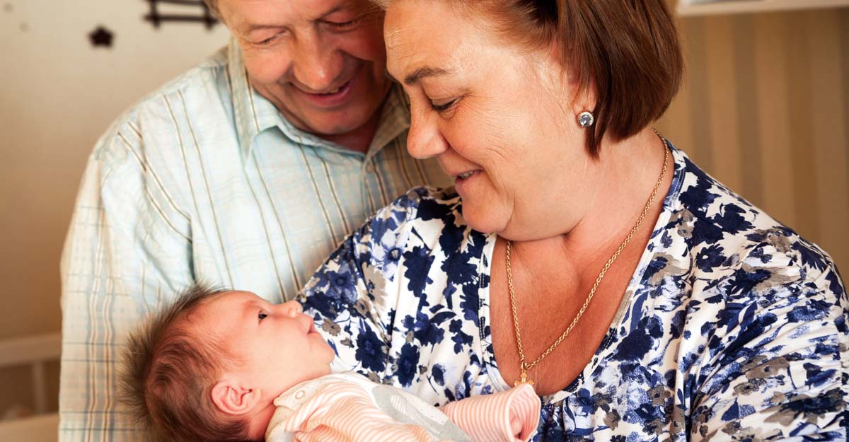 Grandmother holding newborn grandchild with grandfather looking over her shoulder